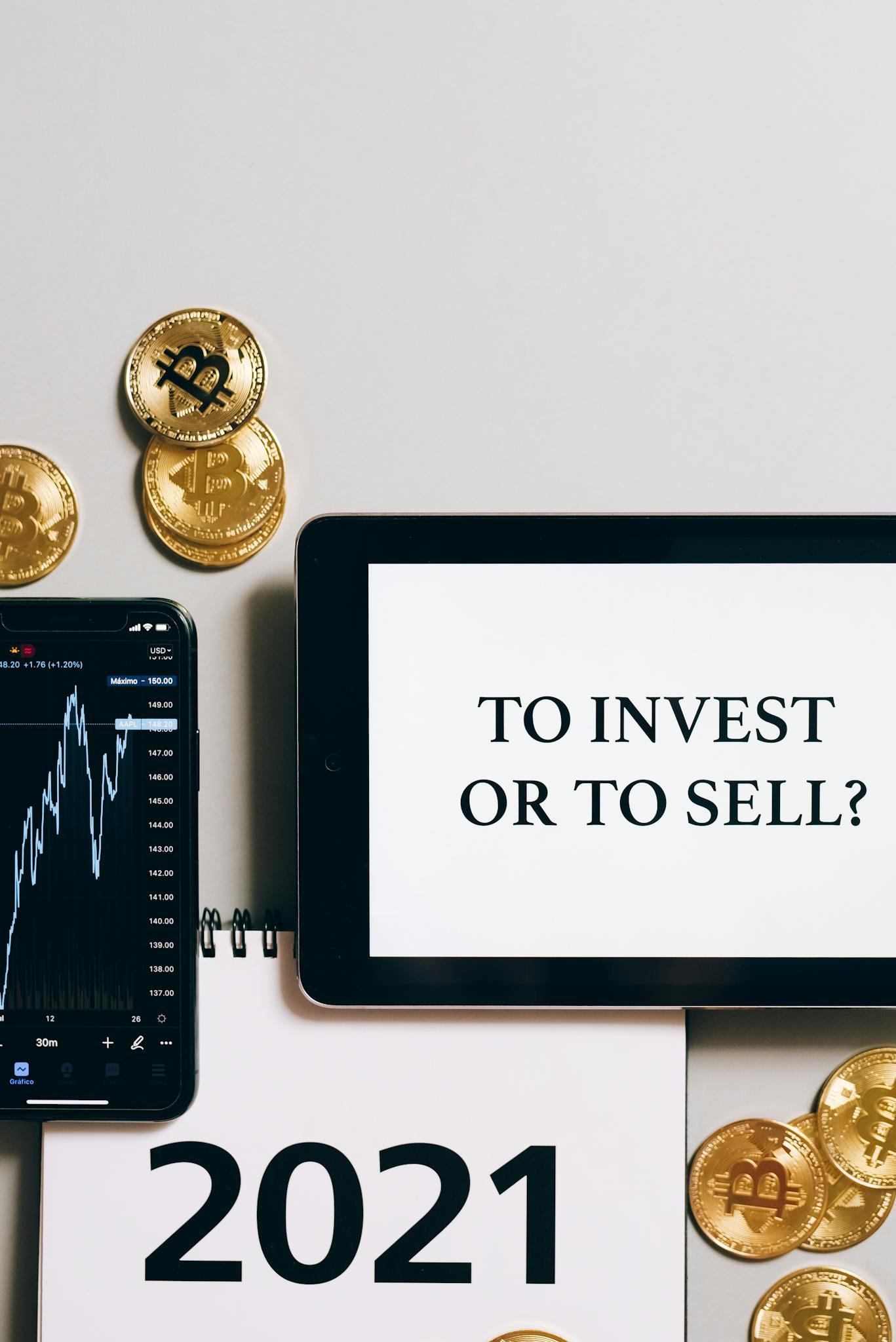 Home 1 Tablet with 'To Invest or To Sell?' text, gold bitcoins, smartphone displaying a stock chart.